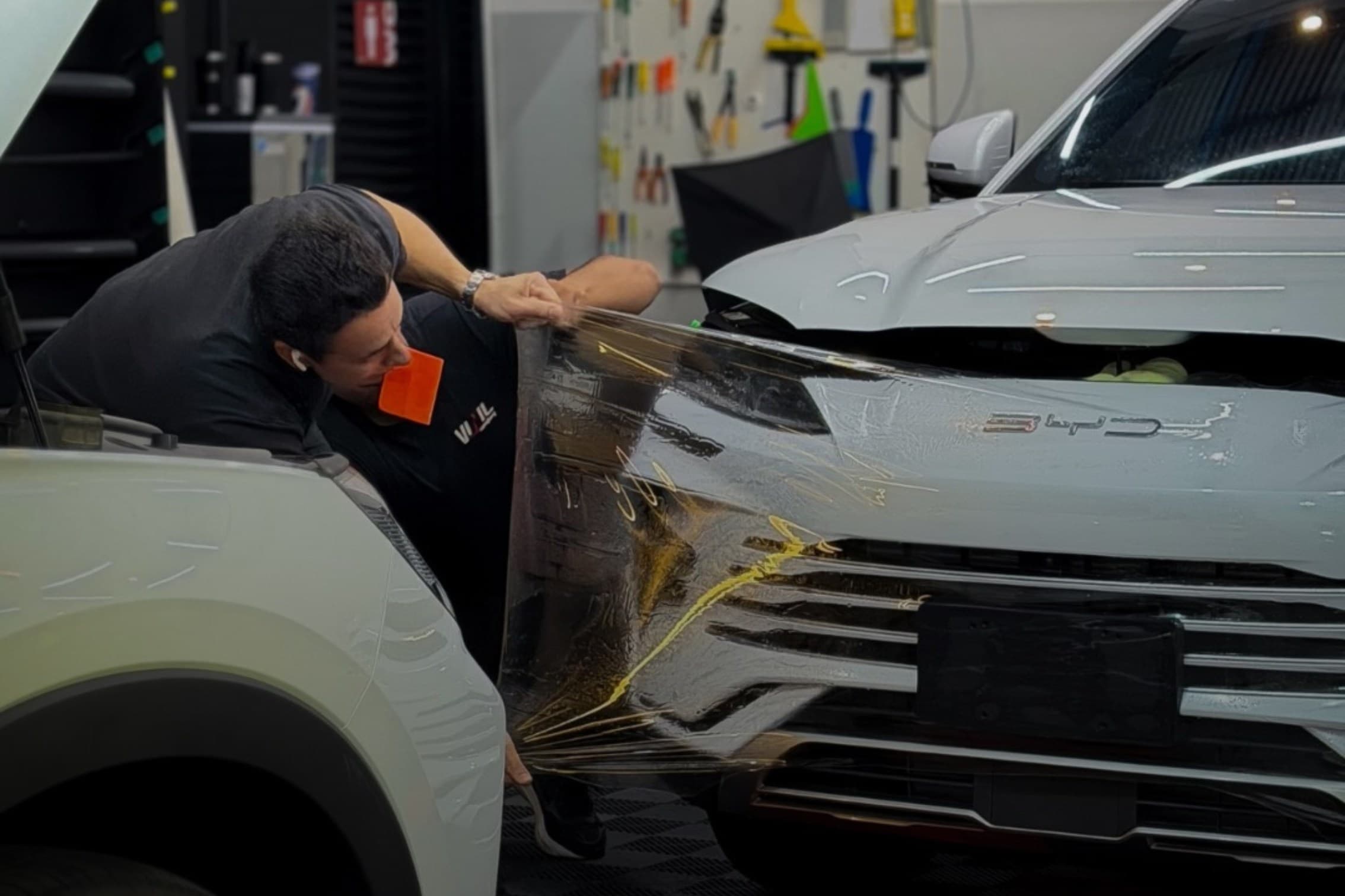 Aplicador instalando película de proteção de pintura no capô de um SUV dentro de uma oficina de estética automotiva