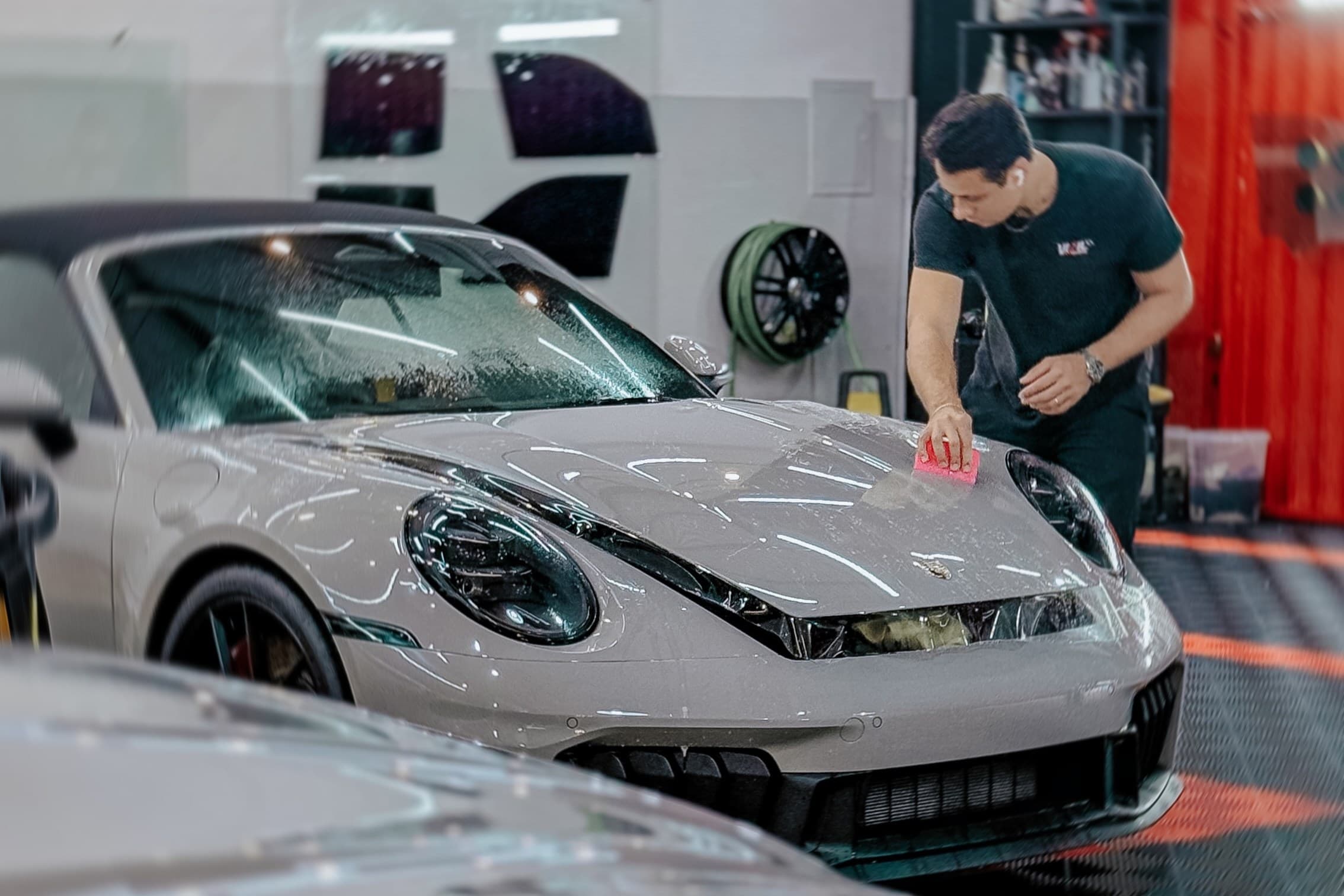 Profissional passando a espátula sobre o capô de um Porsche 911 durante a aplicação da película de proteção